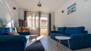 Een moderne woonkamer met een blauwe zithoek, een witte salontafel en een televisie op een houten kast.