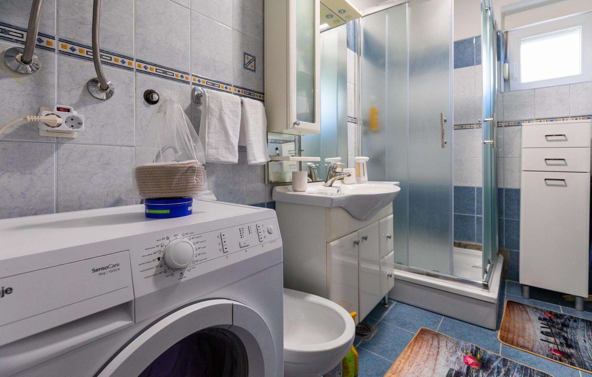 Une salle de bain moderne équipée d’un lave-linge, de toilettes, d’un lavabo et d’une douche à parois de verre.