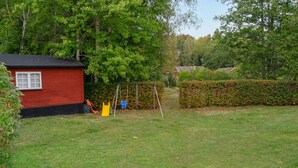 Un bâtiment rouge avec une fenêtre, une balançoire et une haie dans une cour verdoyante.
