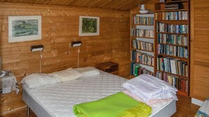 Une pièce chaleureuse aux murs en bois, avec un grand lit, une bibliothèque remplie de livres et deux tableaux encadrés accrochés au mur.