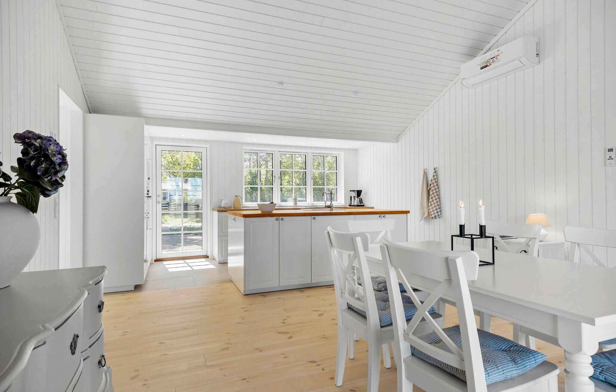 A bright kitchen with white cabinetry, a wooden countertop, and a view through a glass door.
