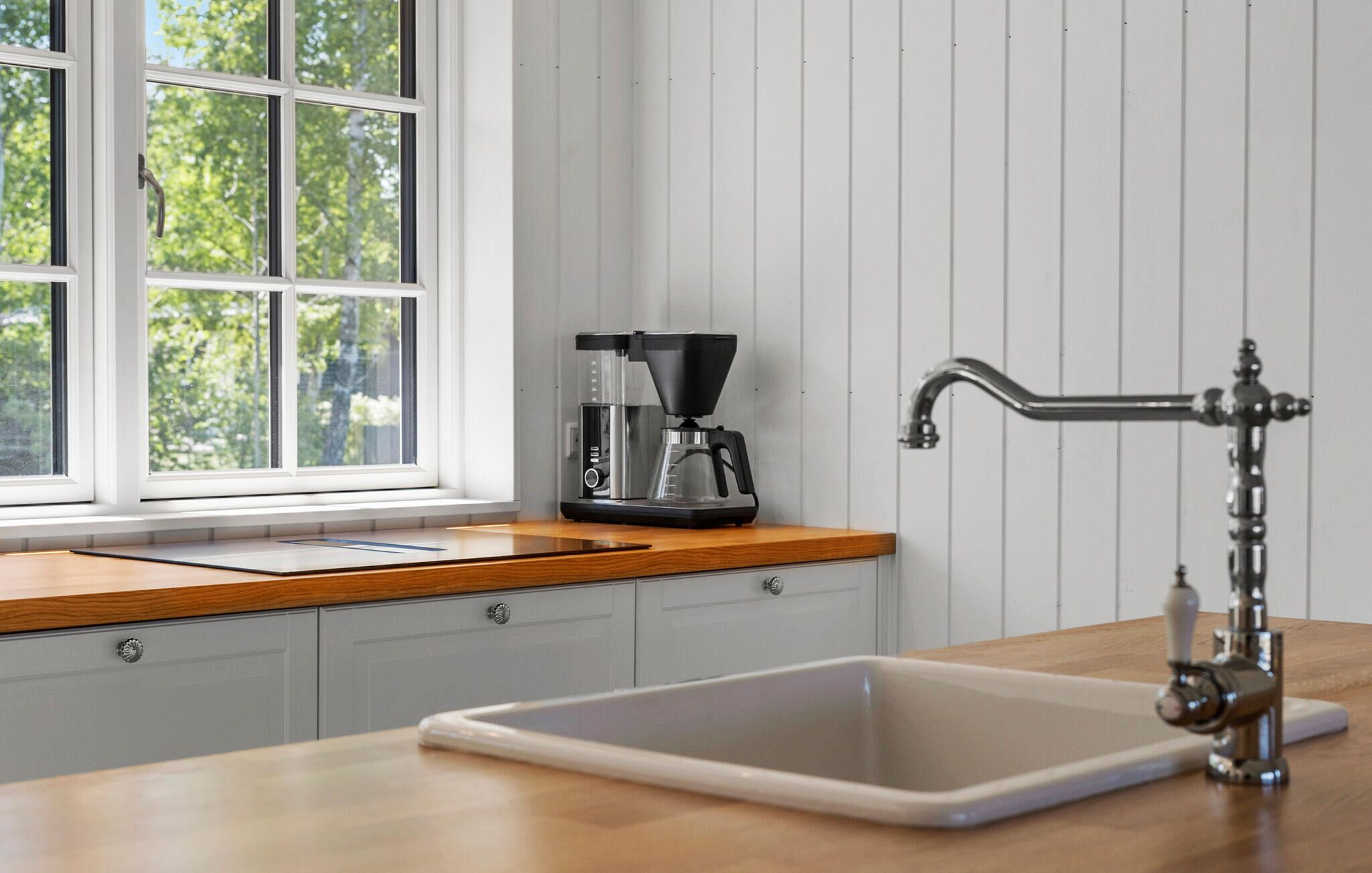 A kitchen with a wooden countertop, a coffee maker, a sink, and a window with a view of trees.