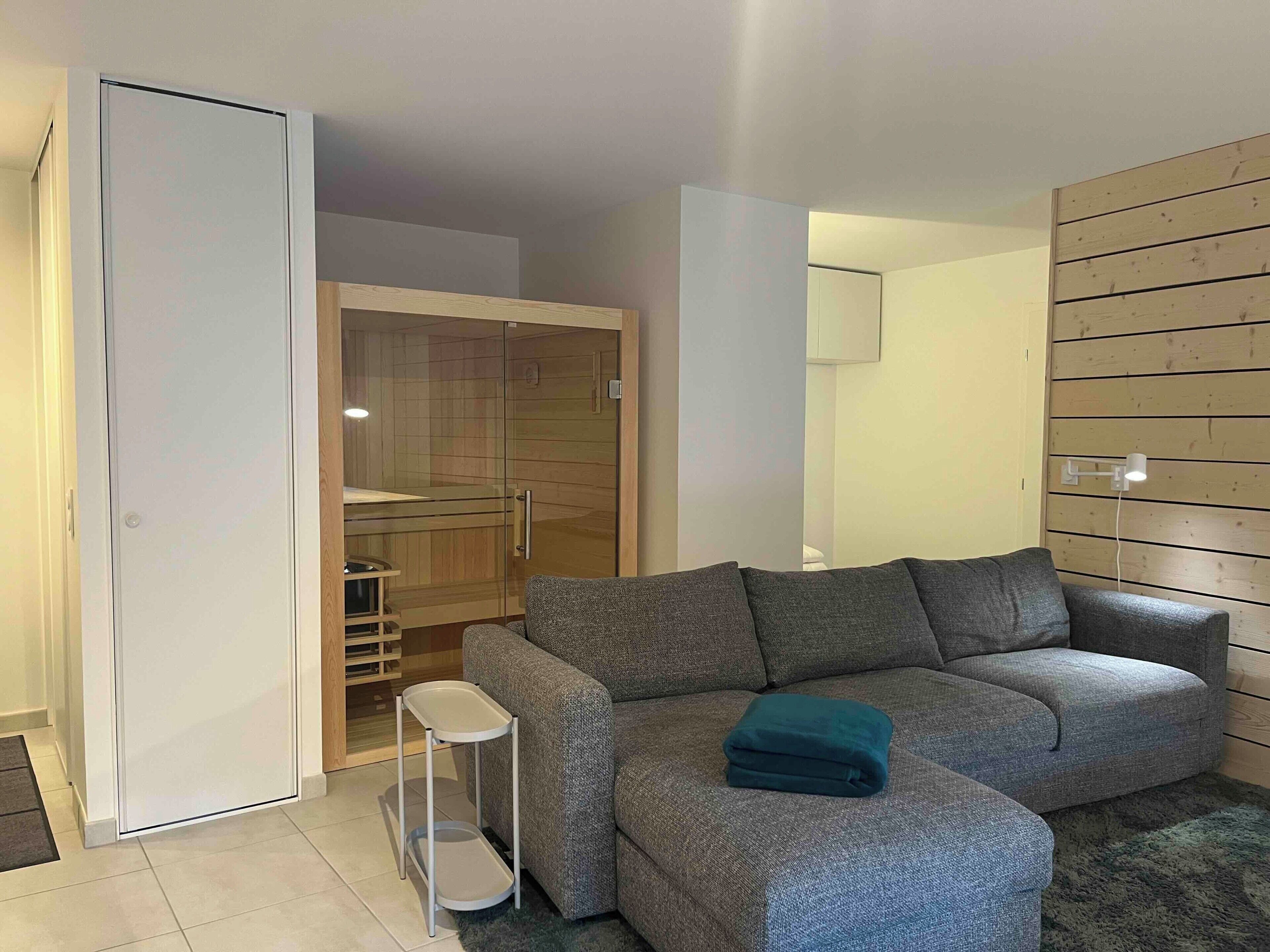 A modern living room with a grey sofa, a small side table, and a wooden wall panel.