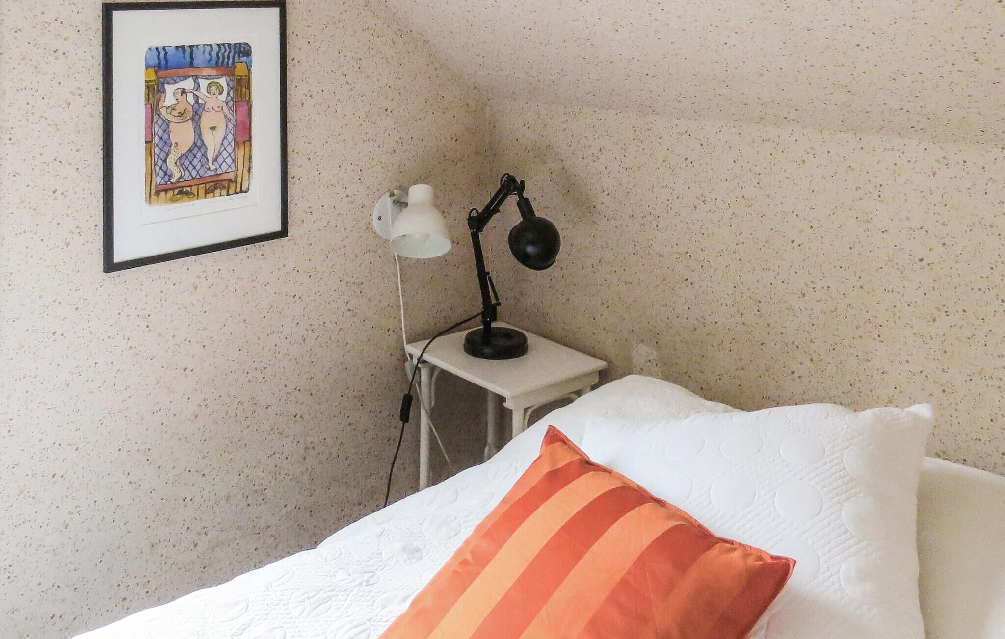 Ein Schlafzimmer mit einem Bett, einem Nachttisch mit Lampe und einem gerahmten Bild an der Wand.