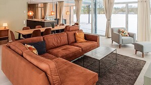Un salon moderne avec un canapé marron, un fauteuil gris et un coin repas doté d’une longue table.
