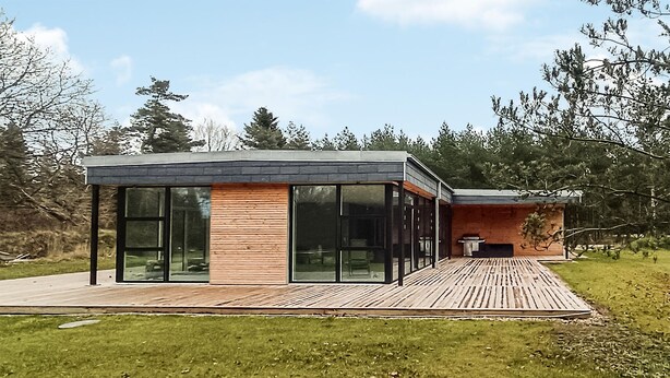 Une maison moderne dotée de grandes baies vitrées, d’une terrasse en bois et d’une façade en briques.