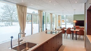Une cuisine moderne dotée d’un grand îlot central, d’un coin repas avec des chaises rouges et de grandes fenêtres ornées de rideaux.