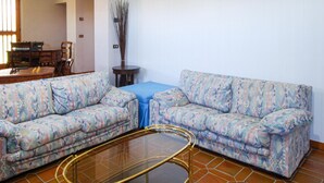A living room with two patterned sofas, a glass coffee table, and a blue tablecloth.