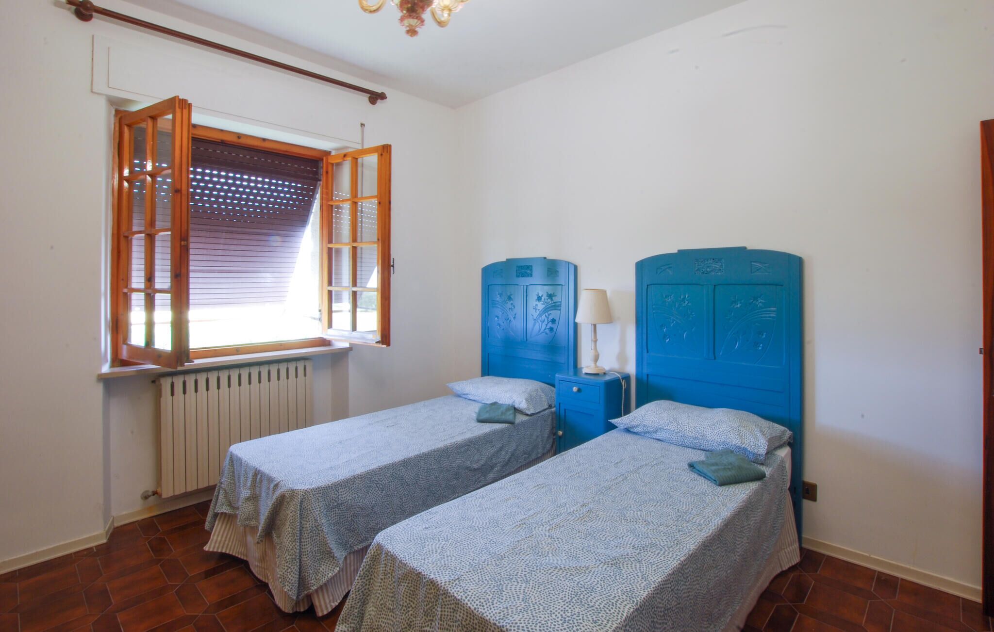 A room with two single beds, a window with blinds, a radiator, and a wooden ceiling.