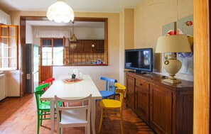 A dining area with a table, chairs, a television, and a lamp.