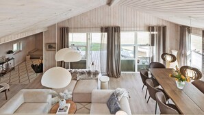 A spacious loft with high ceilings, wooden walls, a cozy seating area, a dining table, and large windows offering a view of the outdoors.