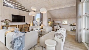 A modern living room with a wooden ceiling, a flat-screen TV, and a cozy seating area with a sofa and armchairs.