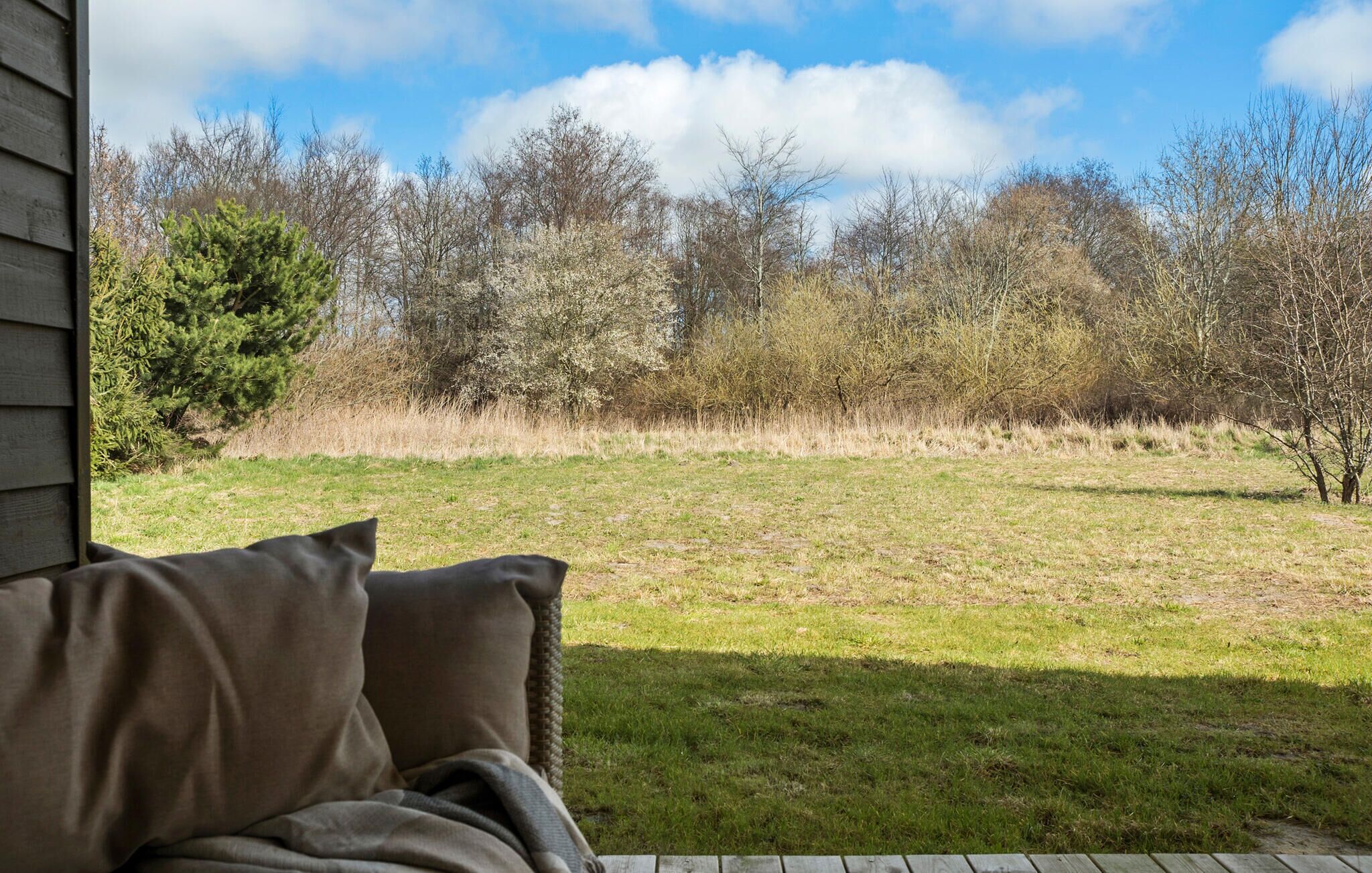 A view from a porch with a wooden deck, overlooking a grassy yard with trees and a clear sky.