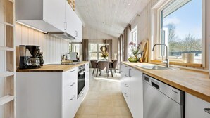 A modern kitchen with white cabinetry, a coffee machine, a dining area with a table and chairs, and a large window providing a view of the outdoors.
