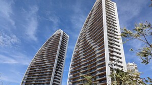 Deux immeubles de grande hauteur, dotés d’une architecture moderne, avec de nombreux balcons et un ciel dégagé en arrière-plan.
