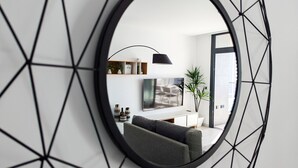 Un salon moderne avec un grand miroir, un téléviseur à écran plat, un canapé et une plante en pot.