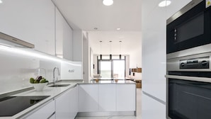 A modern kitchen with white cabinetry, a black oven, and a marble floor.