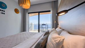 Une chambre d’hôtel moderne dotée d’un grand lit, d’un balcon avec une table et des chaises, et offrant une vue sur la mer.