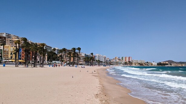 A beach with a sandy shore, palm trees, and buildings along the coastline. - POSIDONIO old town apartment (La Vila Joiosa)