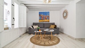 A modern living room with a grey sofa, two small tables, a patterned rug, a painting of a coastal town, and a decorative wall piece. - POSIDONIO old town apartment (La Vila Joiosa)