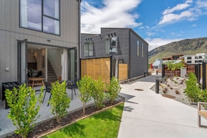 Ein modernes, zweistöckiges Haus mit einer Terrasse, einer Treppe zum oberen Stockwerk und Blick auf eine gebirgige Landschaft.