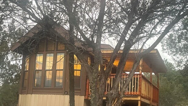 Una cabaña de madera con un ventanal grande, un balcón y un árbol en primer plano.