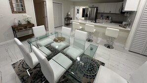 A modern kitchen with white cabinets, stainless steel appliances, and a glass dining table with white chairs. - Charming 4-bedroom house for the entire family (sixth court)