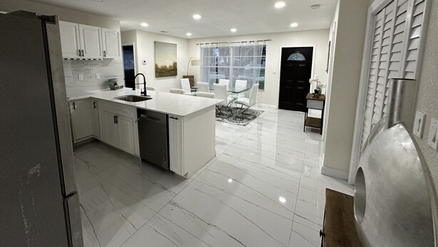 A modern kitchen with white cabinetry, a central island, and a dining area with a glass table and chairs. - Charming 4-bedroom house for the entire family (sixth court)