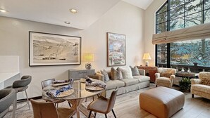 Un salón espacioso con una mesa de comedor de cristal, asientos cómodos y grandes ventanales con vistas al exterior.