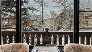Una zona de estar acogedora con dos sillones mullidos y una mesita, con vistas a un balcón nevado con barandilla y árboles.