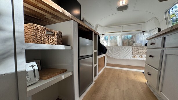 A compact RV kitchen with a toaster, a refrigerator, and a bed with a white canopy.