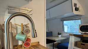 A compact kitchenette with a stainless steel sink, hanging mugs, a toaster, and a small window.
