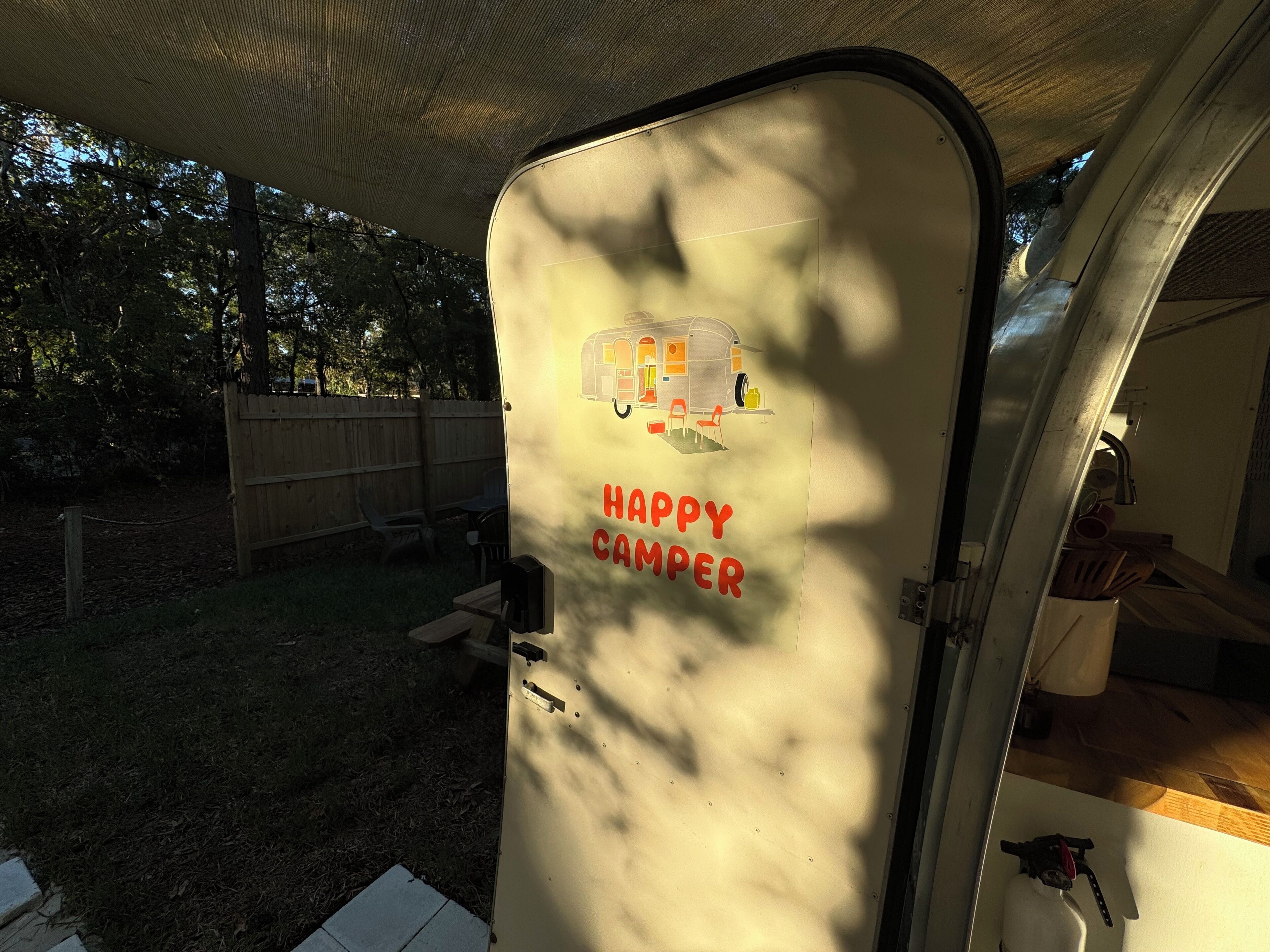 A camper van with a "Happy Camper" decal, a wooden deck, and a fenced backyard.