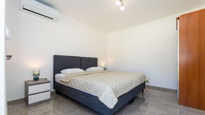 Une chambre à coucher comprenant un lit, des tables de chevet, un appareil de climatisation et une porte en bois.