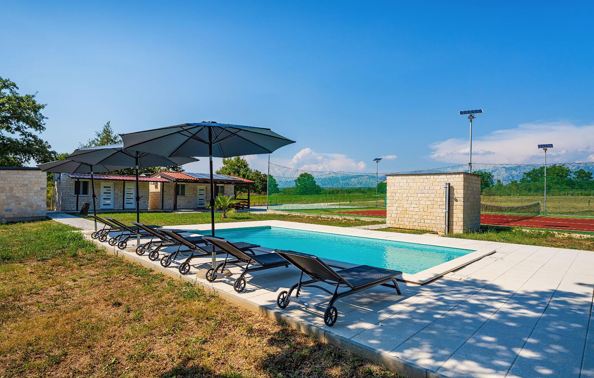 A swimming pool with lounge chairs and umbrellas, a stone building, and a view of mountains.