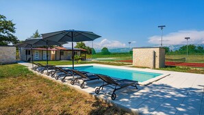 Une piscine avec des chaises longues et des parasols, un bâtiment en pierre et une vue sur les montagnes.