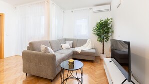Un saló modern amb un sofà seccional gris, una taula de centre rodona, un televisor de pantalla plana i una planta en test.