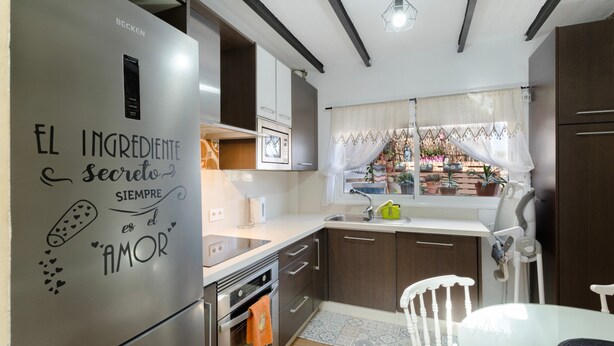 A modern kitchen with a stainless steel refrigerator, wooden cabinets, a built-in oven, and a window with curtains.