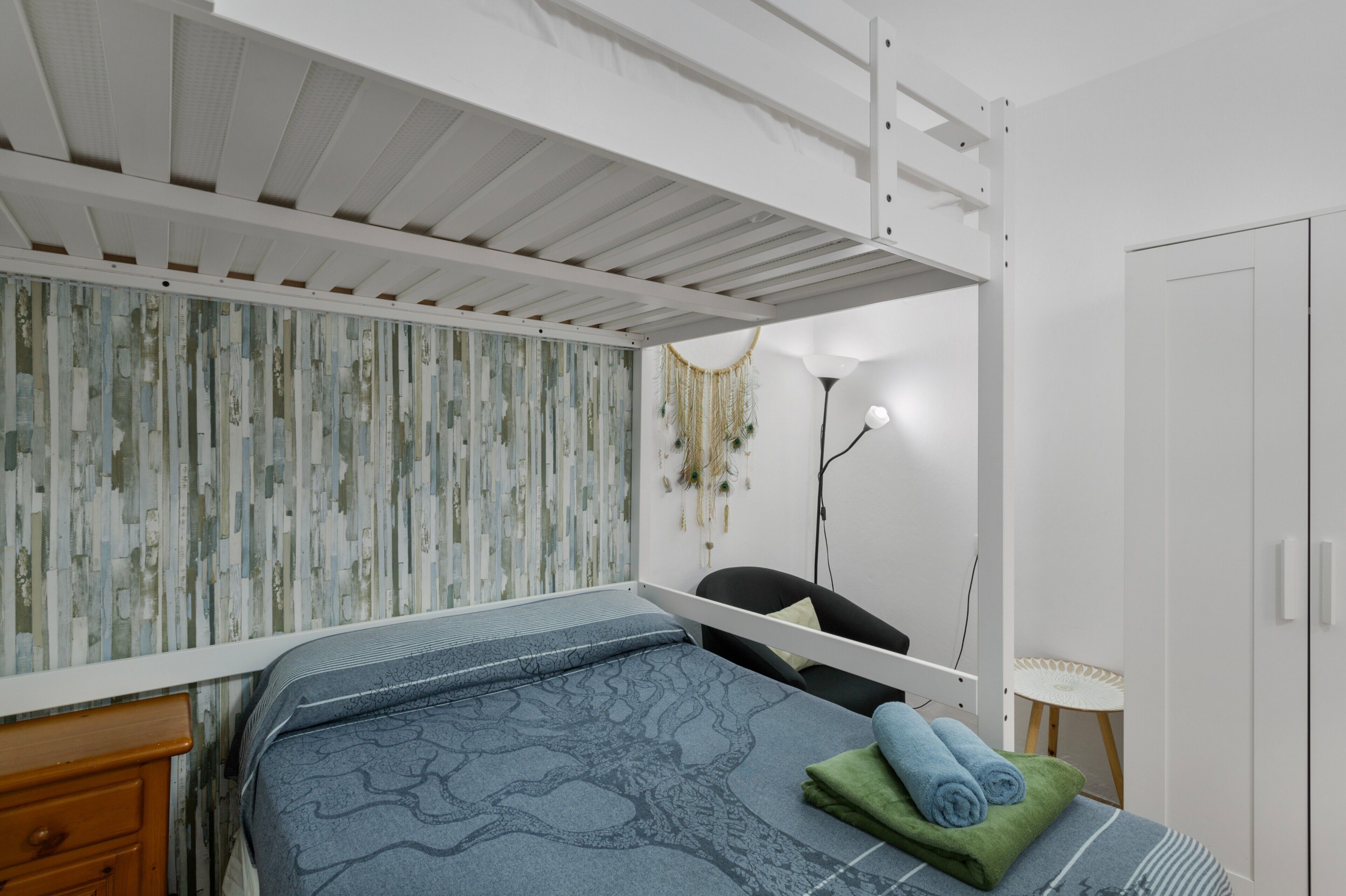 Ein Schlafzimmer mit Etagenbett, Nachttisch, Stuhl, kleinem Tisch und Kleiderschrank.