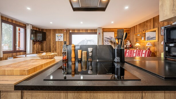 A modern kitchen with wooden paneling, a central island with various kitchen items, a television, and a window with a view. - Holiday Home 'D'Aillon' with Mountain Views, Private Terrace, and Wi-Fi (Aillon-le-Jeune)
