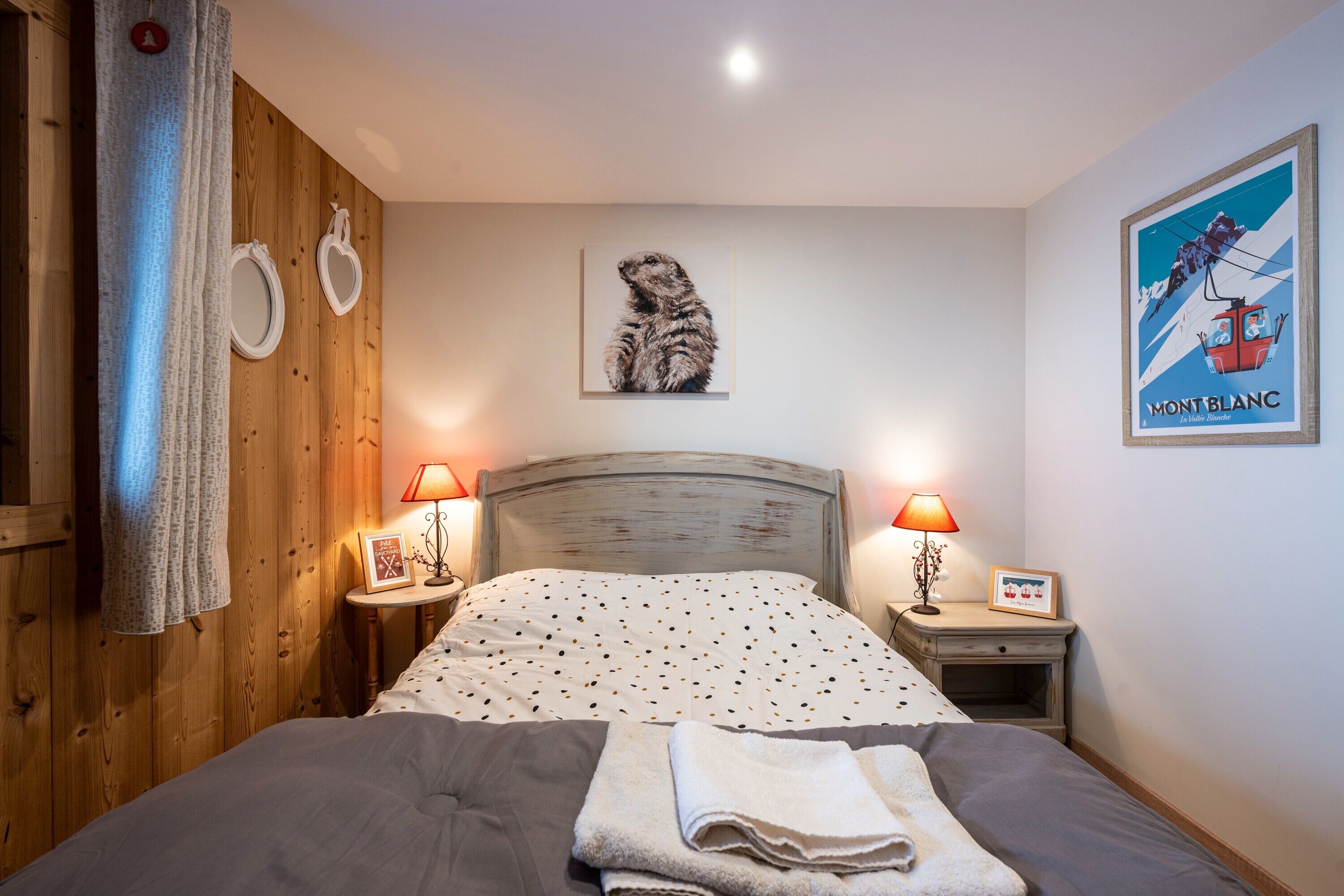 Une chambre à coucher avec un lit, deux lampes de chevet, un tableau encadré au mur et une affiche accrochée au mur.