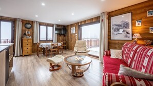 A cozy room with a dining table, chairs, a sofa, a TV, and a large window. - Holiday Home 'D'Aillon' with Mountain Views, Private Terrace, and Wi-Fi (Aillon-le-Jeune)