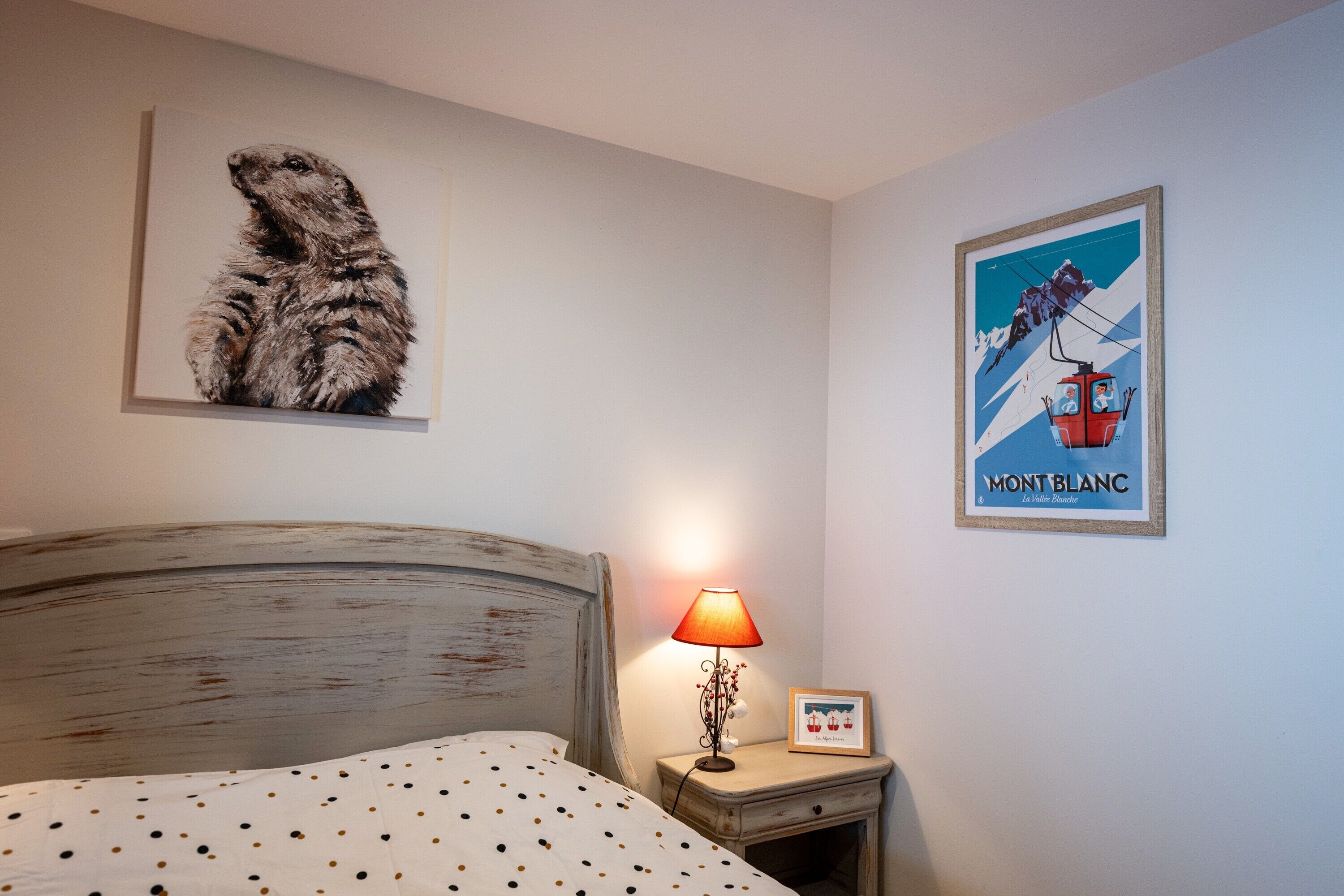 A bedroom with a bed, a nightstand with a lamp, a framed picture of a mountain, and a poster of a mountain.