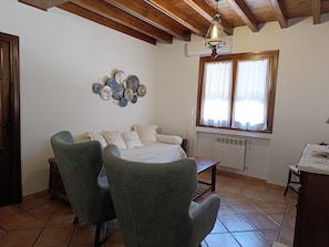 Una habitación con cama, dos sillas, un radiador, una ventana con persianas, un aplique de pared y un ventilador de techo.
