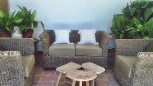 A wicker sofa with cushions, a small wooden table, and potted plants.