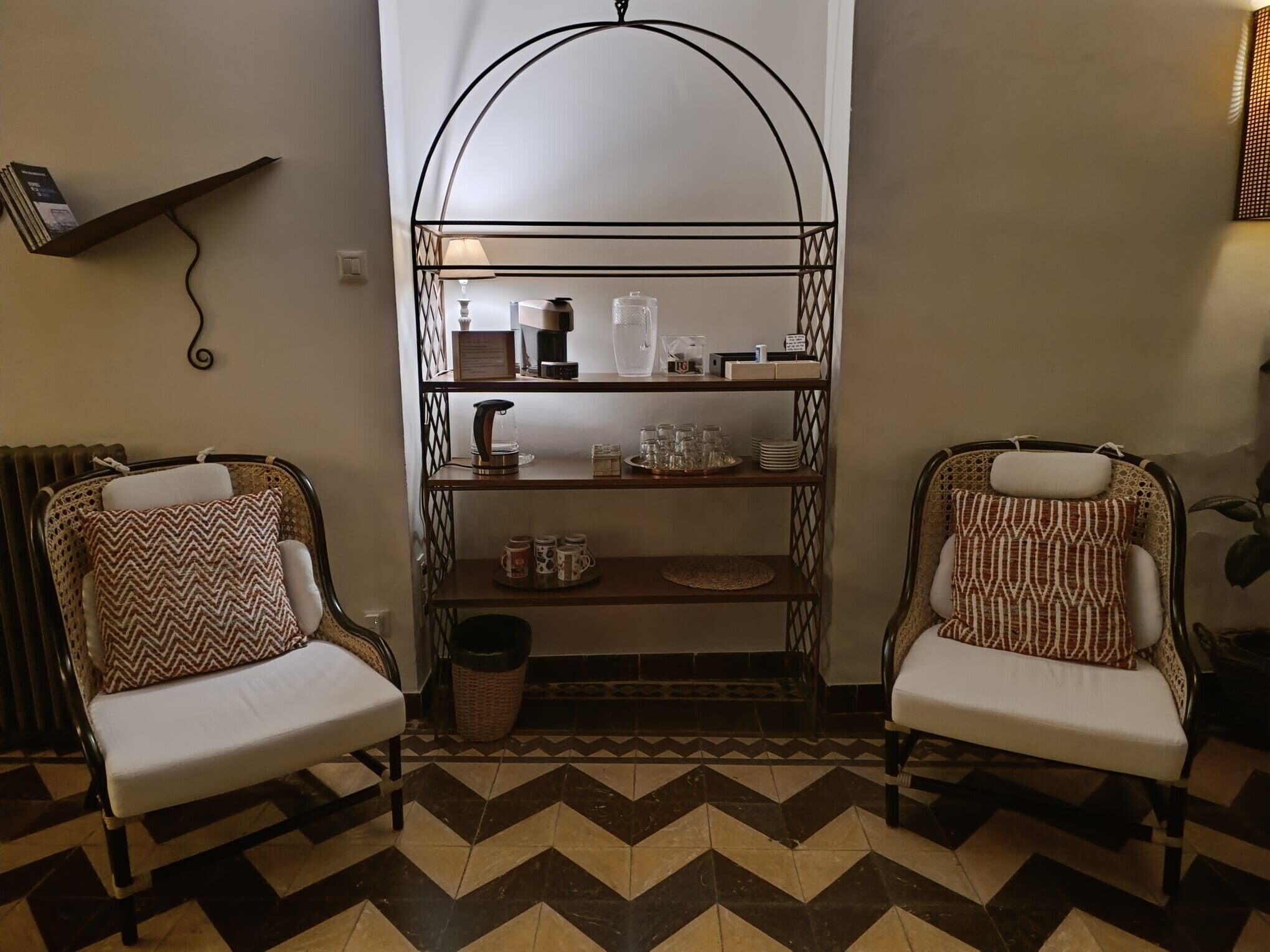 A room with two patterned chairs, a coffee station, and a radiator.