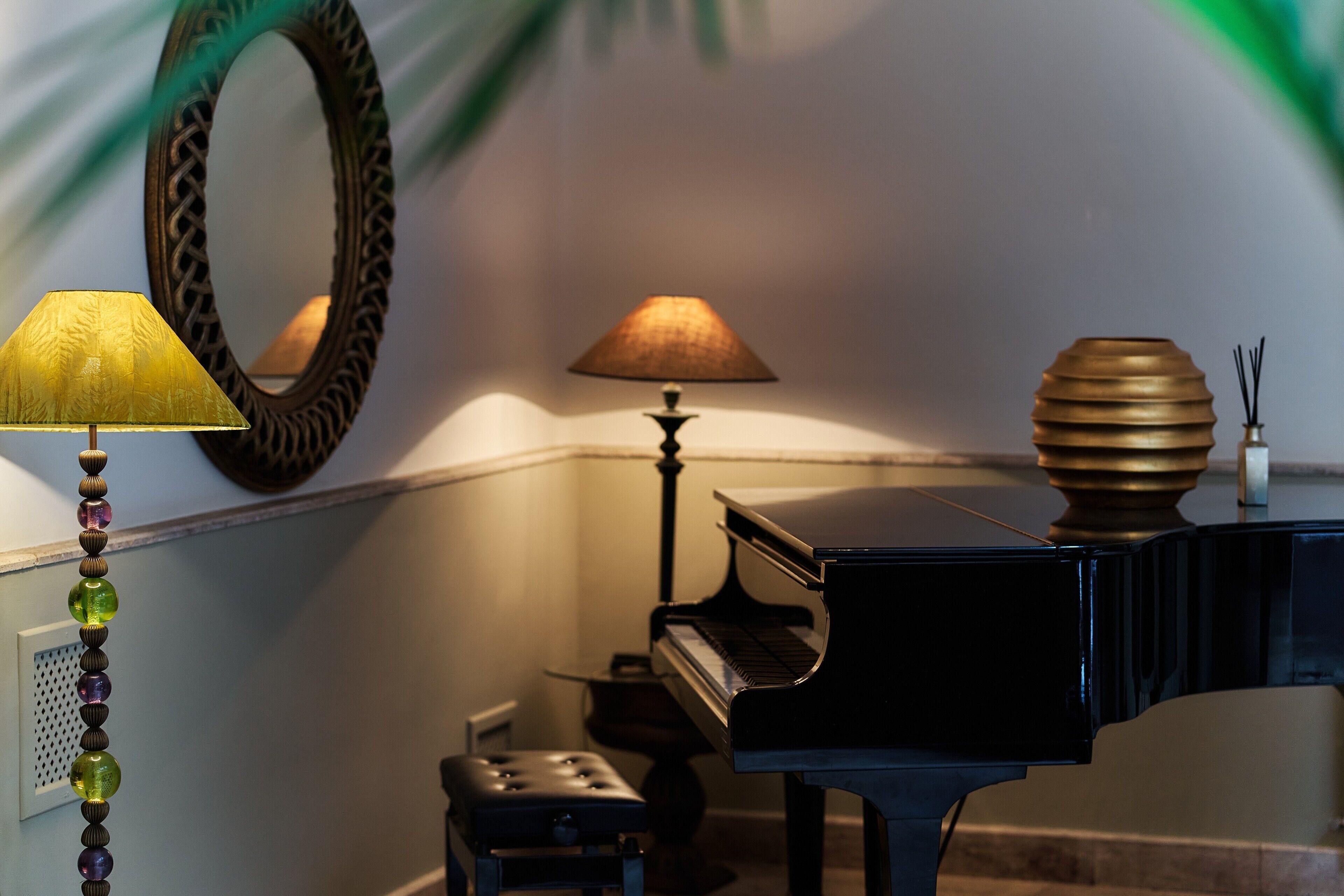 Un pianoforte, una lampada, uno specchio e un vaso decorativo in una stanza.
