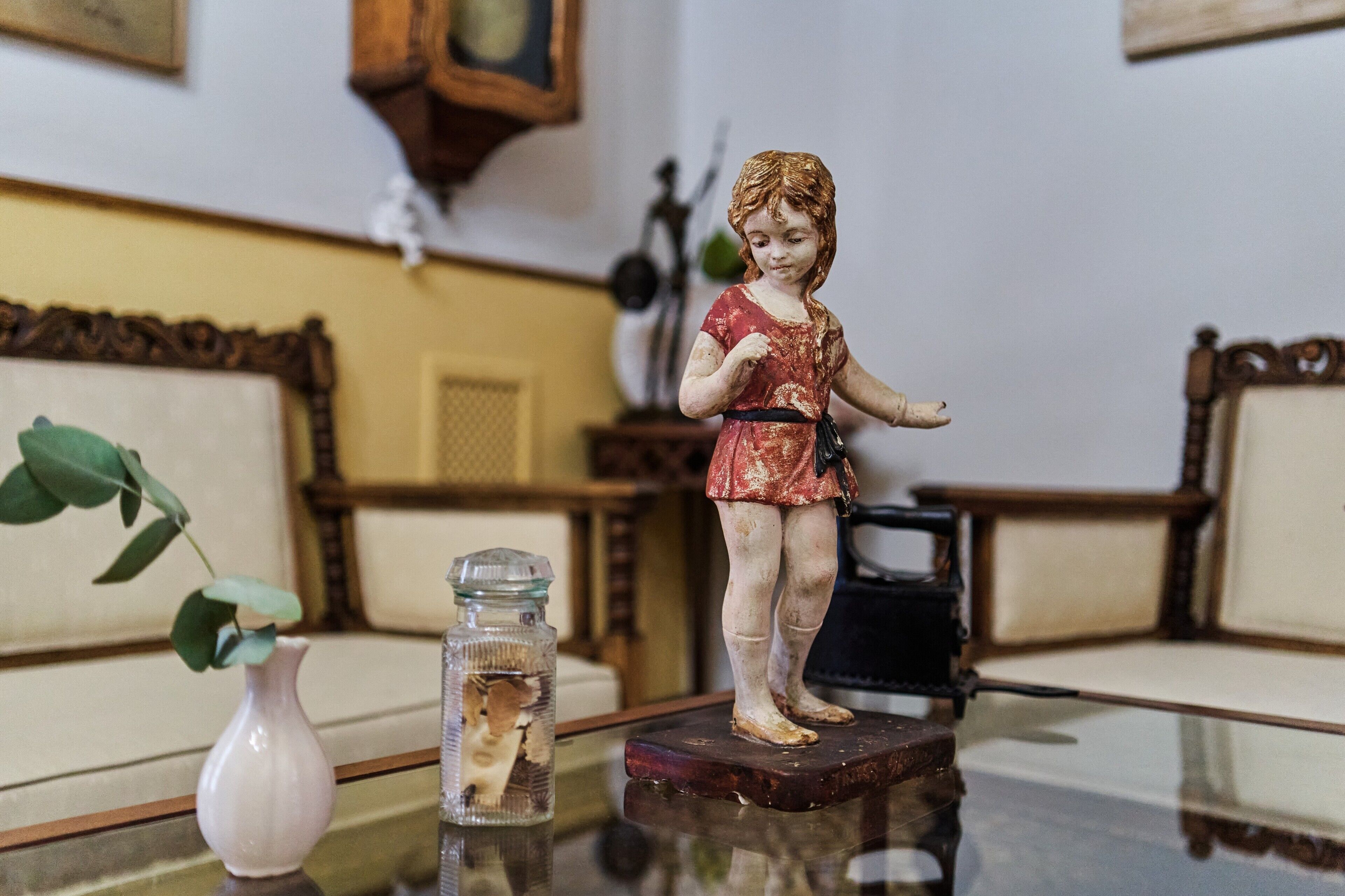 Une figurine posée sur une table, un vase avec une plante et un objet décoratif accroché au mur.