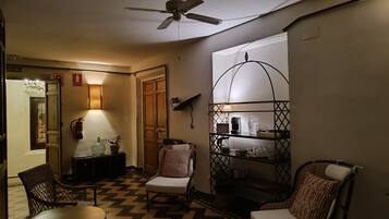 A room with a ceiling fan, a chair, a table, a shelf with items, and a patterned floor.