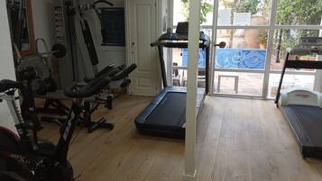 Ginásio com equipamentos de exercício, esteira e porta que dá para o exterior.